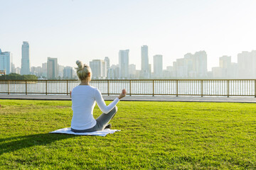 Fototapeta na wymiar Mature woman doing yoga meditation in park at sunrise. Yoga training in city park in Sharjah, UAE.