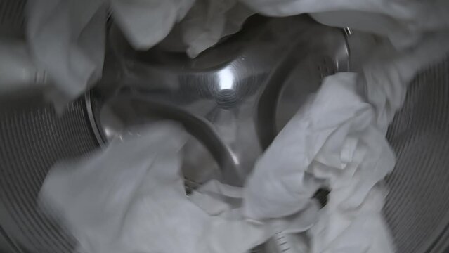 Inside view of the washing machine drum with white clothes, close-up of the drum during the spin cycle.