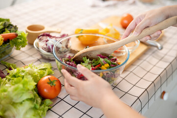 Close-up image of a woman making a fresh and health salad bowl for her breakfast in the kitchen.