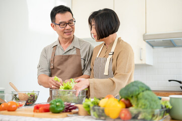 Happy Asian couple, husband and wife, are making a salad bowl in the kitchen together.