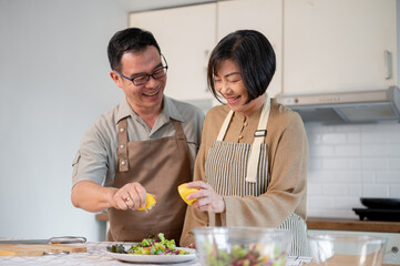 A lovely Asian couple squeezes lemon on a salad plate and enjoys cooking in the kitchen together.