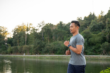A handsome, focused Asian man in sportswear is running outdoors in the morning.