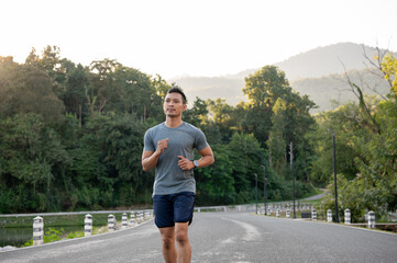 A fit and strong Asian man in sportswear is running on the street in a park in the morning.