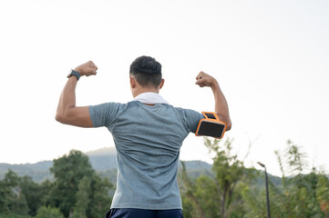 A strong Asian man in sportswear is showing his strong arm muscle, running exercise outdoors.