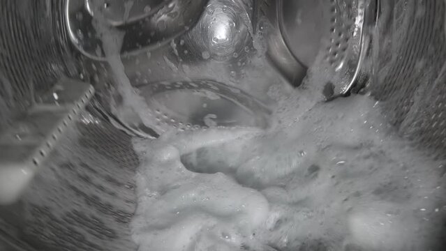 Inside view of the washing machine drum, close-up of the stainless steel drum during the spin cycle, splashing water.
