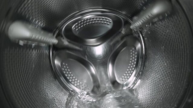 Inside view of the washing machine drum, close-up of the stainless steel drum during the spin cycle, splashing water and foam.