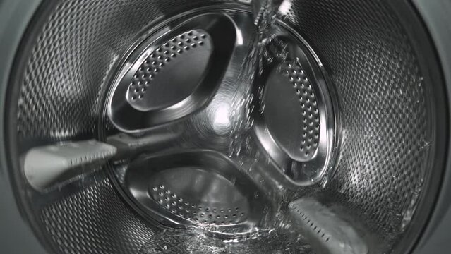 Inside view of the washing machine drum, close-up of the stainless steel drum during the spin cycle, splashing water and foam.