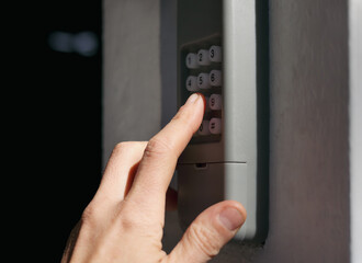 Person using garage door keypad or keyless door access number pad. Gray waterproof box mounted on outside wall of home or building. Used for coded access to open doors or gates. Selective focus.