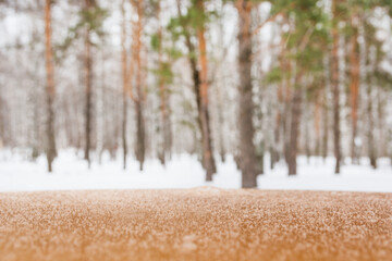 Empty wooden brown tabletop covered with snow with blurred background in winter forest. Winter...