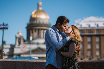 Romantic couple sharing a kiss with an iconic city dome in the blurred background, under a clear sky