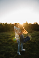 Blurred sunset scene. Young man spins woman walking spending time together in nature. Couple hugging and smiling in grass in field at sunset. Family holiday outdoor. Female embrace male in summer park