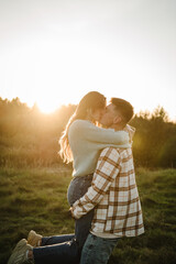 Young man spins woman, walking spending time together in nature. Couple hugging and kissing in grass in field at sunset. Family holiday outdoors. Female embrace male in summer park. Sunset scene.