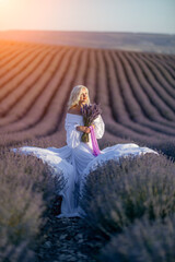 Blonde woman poses in lavender field at sunset. Happy woman in white dress holds lavender bouquet....
