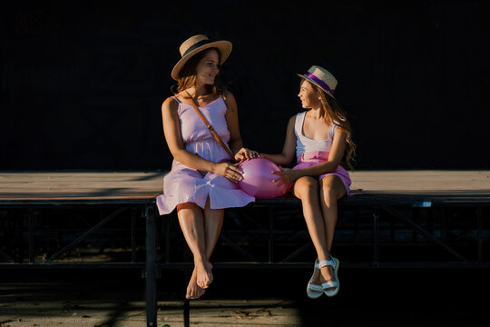 mother and daughter are sitting in pink dresses with flowing long hair on a black background. Enjoy communicating with each other