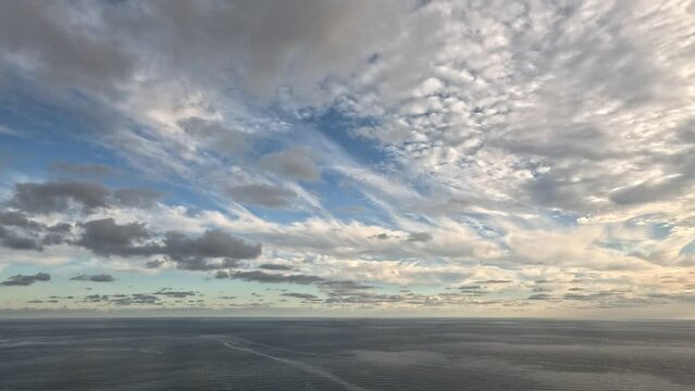 Timelapse multilayered Cirrus and Cumulus clouds moving in bright sunset sky over calm sea. Abstract aerial nature summer ocean sunset, sea and sky view. Vacation, travel. Weather and Climate Change
