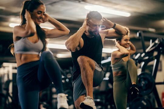 Group of friends doing high knees exercise on a gym with male coach.