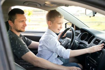 Dad and happy son in the front seat of a car driving a car. The boy holds the steering wheel.