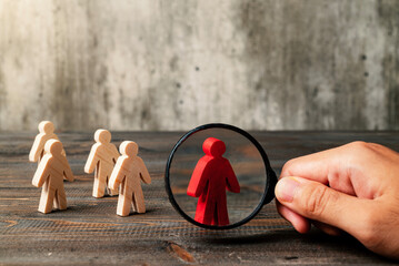 Magnifying glass focuses on a red wooden figure from the crowd of wooden figures