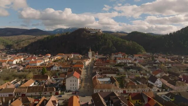 aerial view over orange roofs of city of rasnov and approaching and flying over rasnov fortress in romanian carpathian mountains