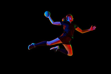 Determined female athlete practicing handball moves with concentration and dedication against black background in neon light. Concept of sport and action, dynamic, victory, championship, ad.