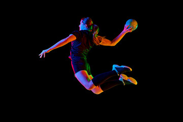 Young female handball athlete practicing throws and receptions against black background in neon...