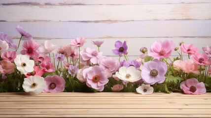 Blooming anemones in various shades of pink, red, and purple spread across a wooden empty table, with a soft-focus background copy space