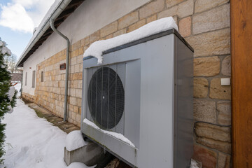 Air heat pump beside house in winter against sandstone wall
