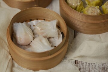 Various type of dim sum in bamboo streamer, such as har gow or hakau, shumai or siomay, tofu skin roll, spring roll and fried noodle shumai. Served with chili oil sauce.