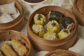 Various type of dim sum in bamboo streamer, such as har gow or hakau, shumai or siomay, tofu skin roll, spring roll and fried noodle shumai. Served with chili oil sauce.