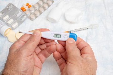 Hand holding a digital thermometer on a background of pills and drugs