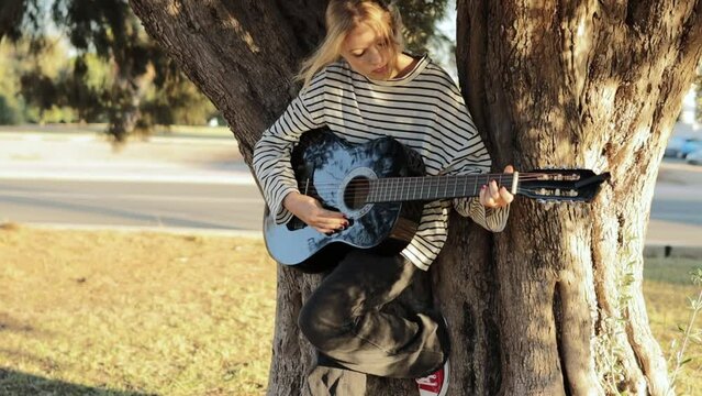 Young attractive woman playing acoustic guitar in a summer park. Woman with happy emotion concept. Slow motion. High quality FullHD footage