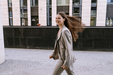 Confident woman in a grey suit strides forward with her hair blowing in the breeze, urban setting