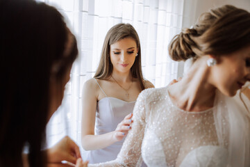 Morning of the bride. The bride's maid of honor helps the bride lace up her dress, fasten buttons on the dress or sleeves. Girlfriends help the bride fasten her dress