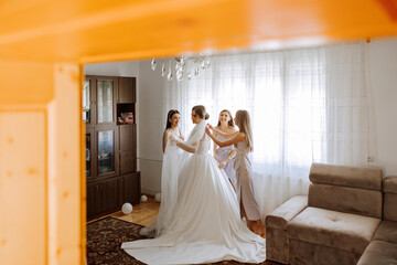 Fototapeta premium Friends rejoice with the bride in the morning. They take pictures, smile, help the bride fasten her dress.
