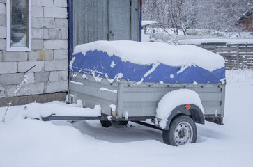 A trailer for a car covered with an awning in the snow. Transportation of belongings.