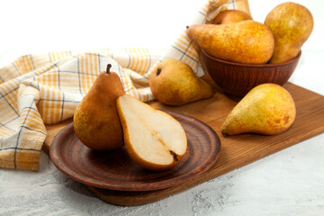 Clay plate with whole and half of pear, wicker basket and yellow kitchen towel on wooden cutting board..