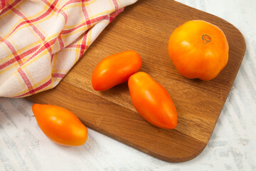 Cutting board with several yellow tomatoes and red kitchen towel on white wooden background..
