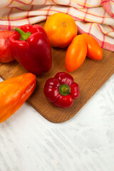 Cutting board with assort of different tomatoes and bell pepper on white wooden background..