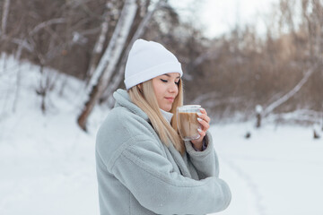 A beautiful young girl smiling and enjoying drinking coffee in a winter forest.
