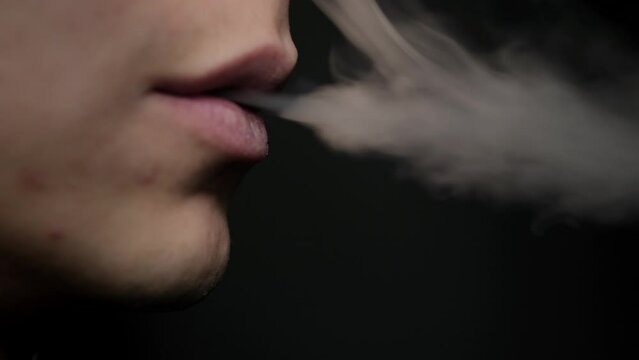 The guy smokes a vape. Close up on a black background. Nicotine addiction concept. Lips exhale smoke
