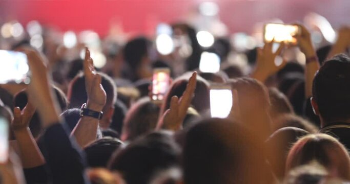 Crowded people in a night party concert view. Young celebrating guys dancing and clapping hands in joyfull concert taking photos and videos for social media sharing. 