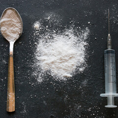 White powder, spoon and syringe on a black background