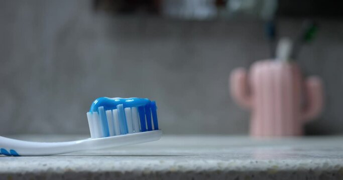 Applying toothpaste to toothbrush, close up. Doctor-approved toothpaste applied to orthodontically correct brush lying on table, bathroom cabinet. Dental health, oral care, brushing teeth concept.