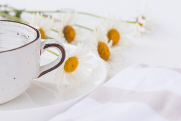 Close up of beautiful chamomile flowers and a white ceramic cup on white plate. Summer table...