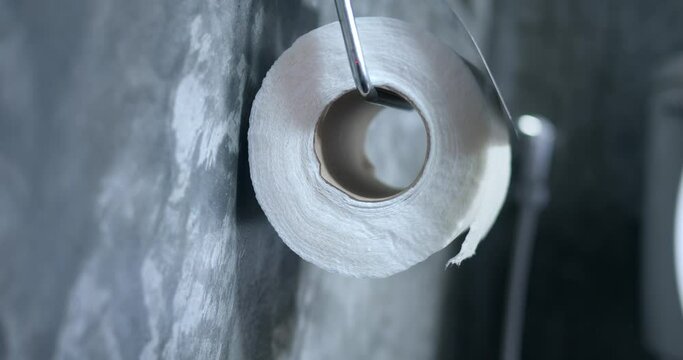 Hand tears off toilet paper in holder. Unwise consumption of toilet paper, too much paper needed when using toilet wc bathroom, washroom. Close Up male hand, steel paper holder on gray bathroom wall
