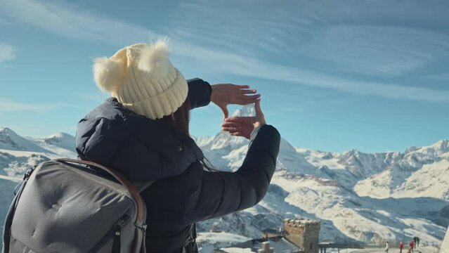Back view of young traveler girl standing over snowy mountain peaks and making frame gesture by hands with Matterhorn Switzerland, Winter traveling scene and planning