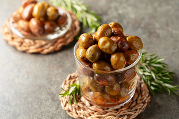 Spicy olives in a glass bowl on a stone table.