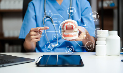 Dentist sitting at table with jaw samples tooth model and working with tablet and laptop in dental...