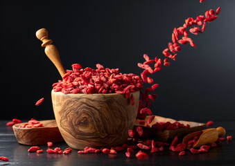 Dried goji berries in wooden bowl on a black background.