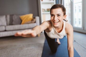 Fototapeta na wymiar Joyful 30-Year-Old Woman with Short Hair Laughing While Doing Yoga in the Living Room